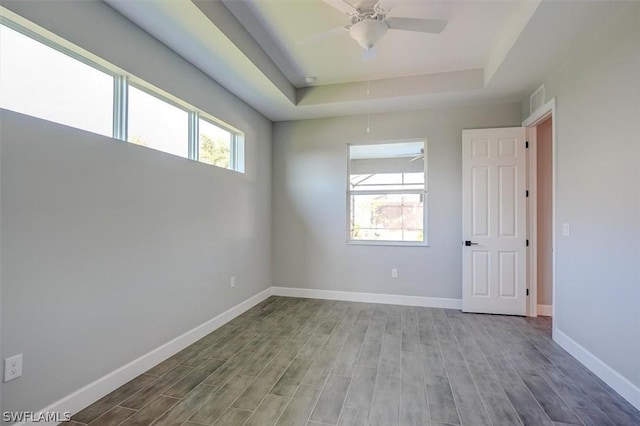 unfurnished room with hardwood / wood-style floors, plenty of natural light, a raised ceiling, and ceiling fan