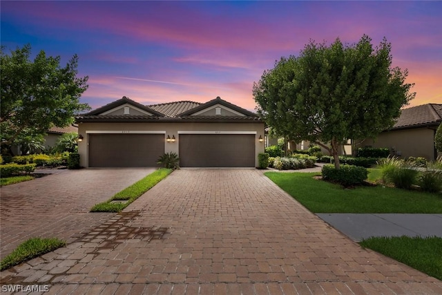 view of front of home with a tiled roof, stucco siding, an attached garage, and decorative driveway