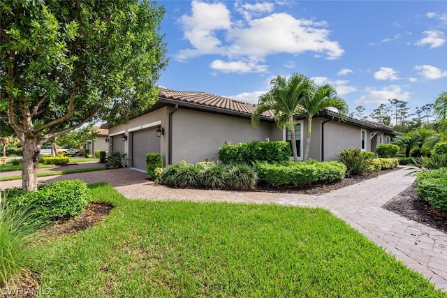 view of home's exterior featuring a tiled roof, stucco siding, decorative driveway, a yard, and an attached garage