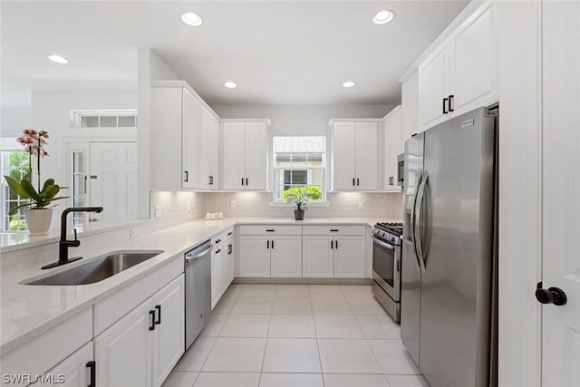 kitchen with a sink, white cabinetry, stainless steel appliances, light tile patterned flooring, and decorative backsplash