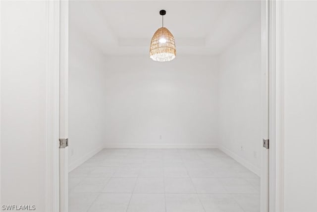 empty room featuring a tray ceiling and baseboards