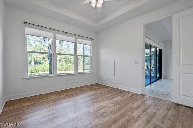 empty room featuring a tray ceiling, baseboards, light wood-style flooring, and a ceiling fan