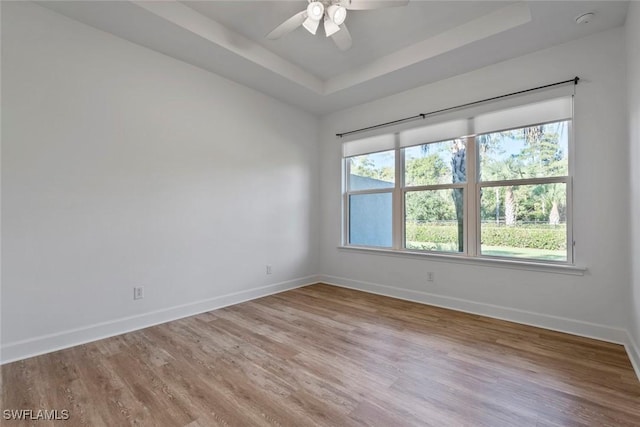 spare room with a tray ceiling, baseboards, ceiling fan, and light wood finished floors