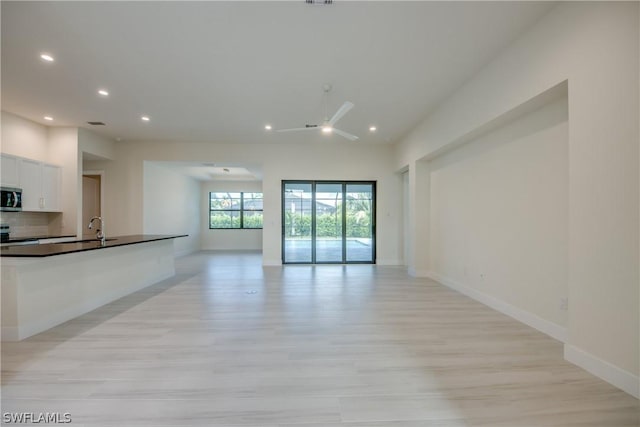 unfurnished living room featuring ceiling fan, sink, and light wood-type flooring