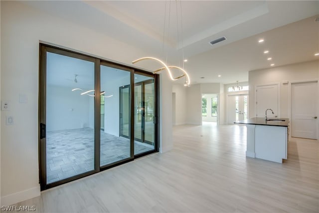 unfurnished room featuring sink, light wood-type flooring, french doors, and a raised ceiling