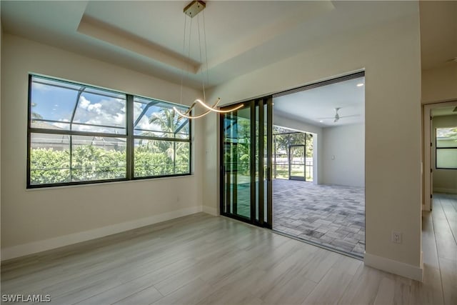 empty room featuring a notable chandelier, a raised ceiling, and a healthy amount of sunlight