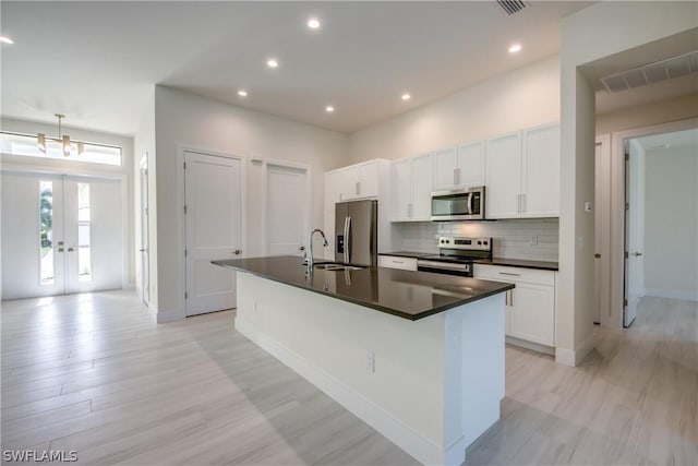 kitchen with pendant lighting, appliances with stainless steel finishes, white cabinetry, sink, and a center island with sink