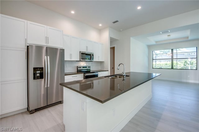 kitchen featuring appliances with stainless steel finishes, tasteful backsplash, sink, white cabinets, and an island with sink