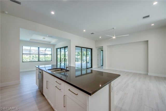 kitchen with a kitchen island with sink, stainless steel dishwasher, white cabinets, sink, and light hardwood / wood-style flooring