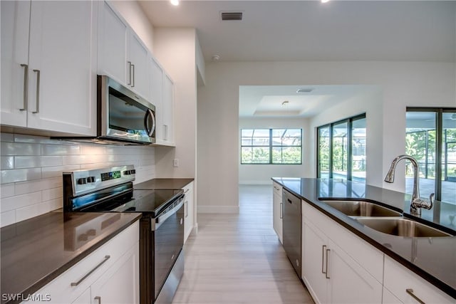 kitchen featuring appliances with stainless steel finishes, tasteful backsplash, white cabinetry, sink, and light hardwood / wood-style flooring