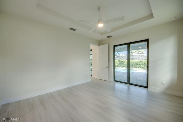 empty room with ceiling fan, a tray ceiling, and light wood-type flooring