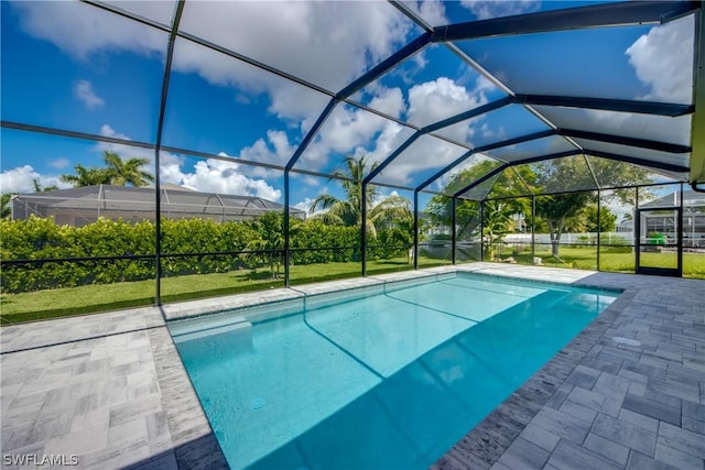 view of pool with a patio, glass enclosure, and a lawn