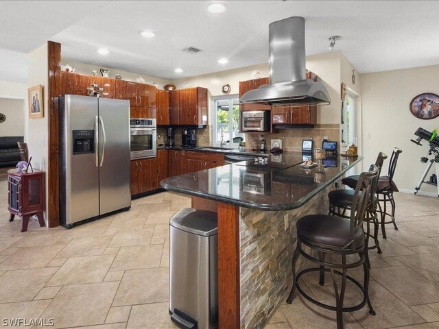 kitchen featuring island range hood, a peninsula, visible vents, appliances with stainless steel finishes, and tasteful backsplash