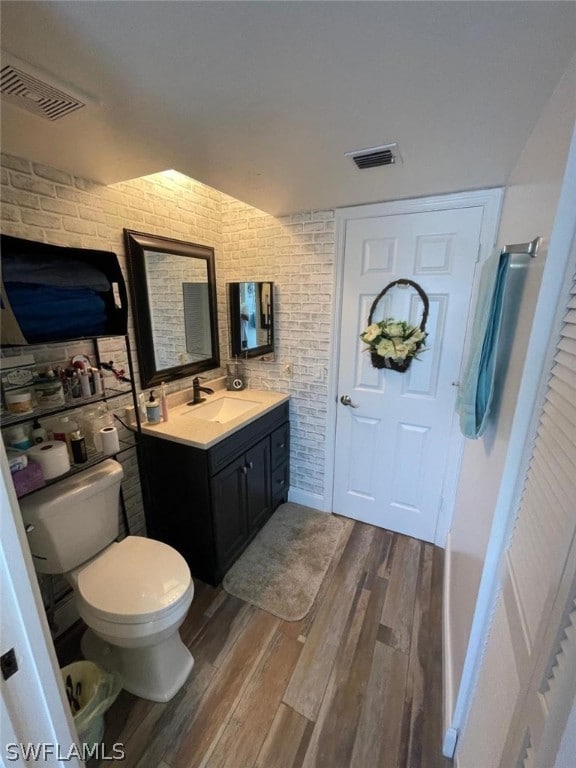 bathroom with hardwood / wood-style floors, oversized vanity, toilet, and brick wall