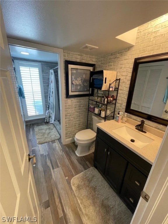 bathroom with brick wall, wood-type flooring, vanity, and toilet