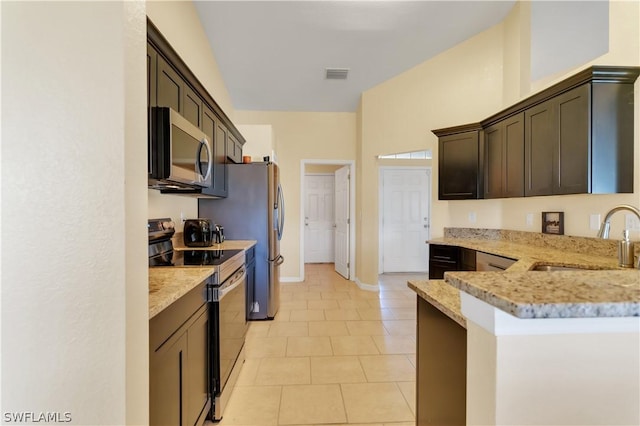 kitchen with appliances with stainless steel finishes, light stone counters, dark brown cabinets, and sink