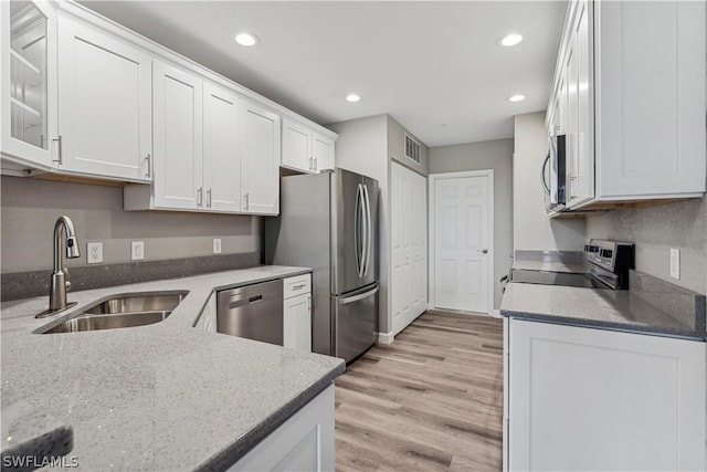 kitchen with appliances with stainless steel finishes, white cabinetry, sink, light stone countertops, and light wood-type flooring