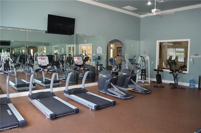 workout area featuring crown molding, baseboards, a high ceiling, arched walkways, and a ceiling fan