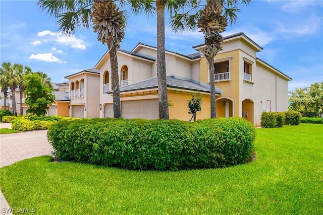 mediterranean / spanish home with stucco siding, driveway, a front yard, a garage, and a balcony