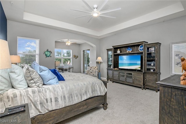 bedroom featuring a tray ceiling, carpet floors, arched walkways, and ceiling fan