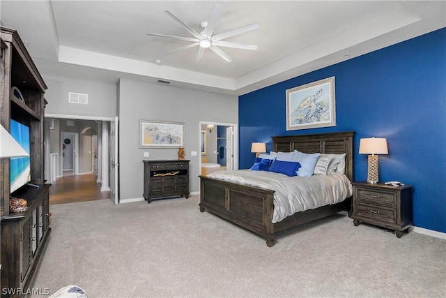 carpeted bedroom featuring visible vents, connected bathroom, baseboards, a raised ceiling, and a ceiling fan