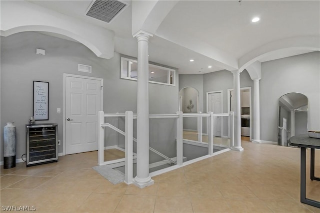 hallway featuring light tile patterned floors, decorative columns, and beverage cooler