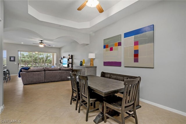 dining area with a tray ceiling, baseboards, arched walkways, and ceiling fan