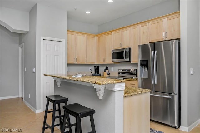 kitchen featuring light stone countertops, a kitchen breakfast bar, light brown cabinetry, light tile patterned flooring, and appliances with stainless steel finishes