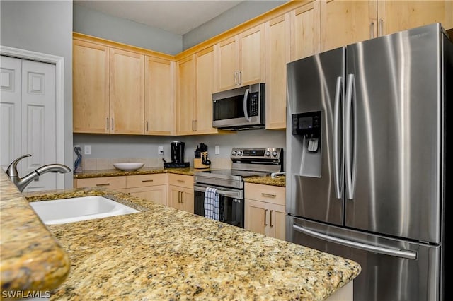 kitchen with light brown cabinetry, light stone countertops, stainless steel appliances, and a sink