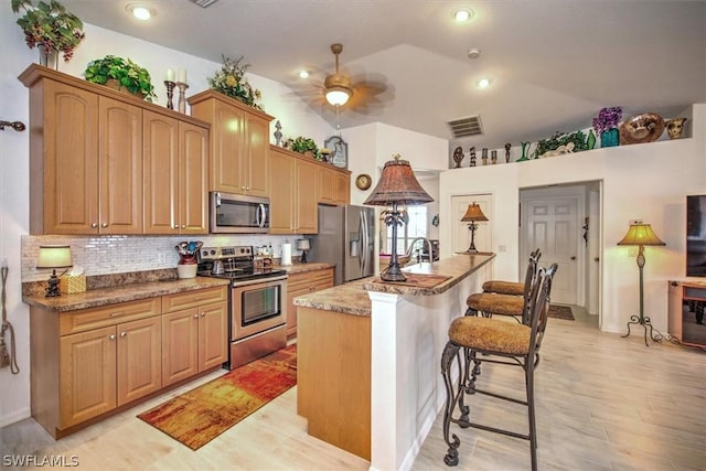 kitchen with a breakfast bar, lofted ceiling, an island with sink, tasteful backsplash, and stainless steel appliances