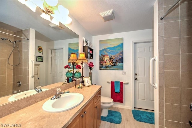 bathroom with a textured ceiling, vanity, tiled shower, hardwood / wood-style flooring, and toilet