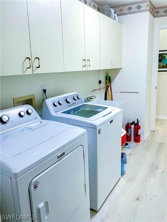 clothes washing area with light wood-style flooring, washing machine and dryer, cabinet space, and baseboards