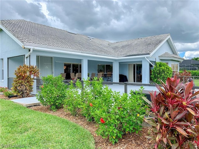 back of house with a tile roof and stucco siding