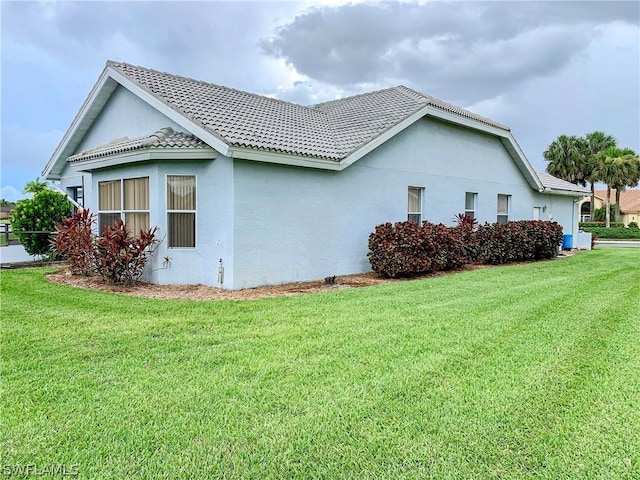 view of side of home with a tile roof, a lawn, and stucco siding