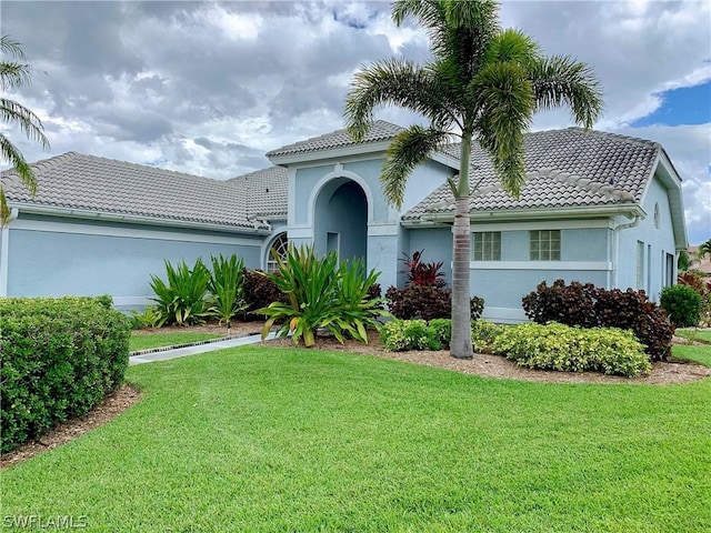 mediterranean / spanish home featuring a tiled roof, a front lawn, and stucco siding