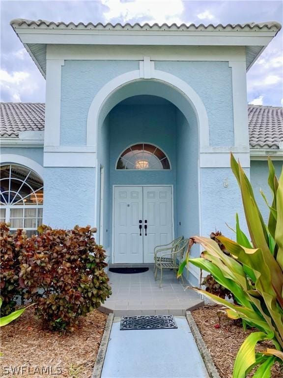 doorway to property featuring a tile roof and stucco siding