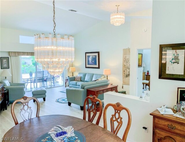 dining area with light hardwood / wood-style floors, high vaulted ceiling, and a notable chandelier