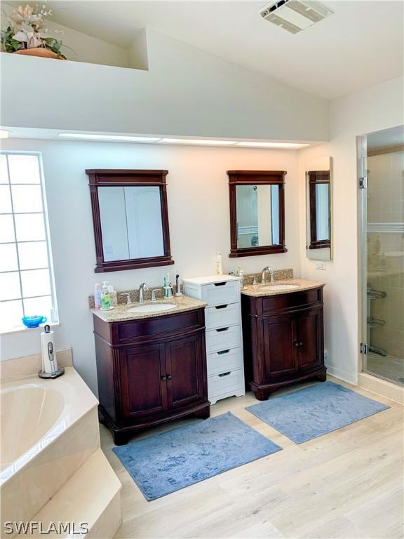 bathroom with hardwood / wood-style flooring, lofted ceiling, plus walk in shower, and double sink vanity