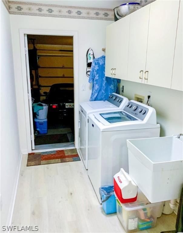 clothes washing area featuring cabinets, washer hookup, light wood-type flooring, washer and dryer, and sink