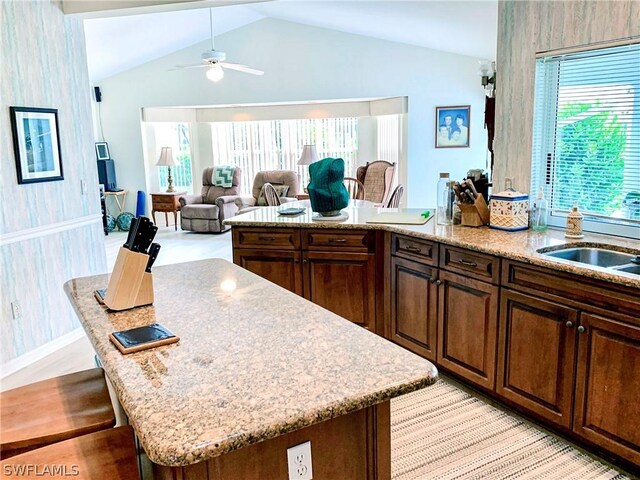 kitchen with a kitchen island, light stone countertops, ceiling fan, and lofted ceiling