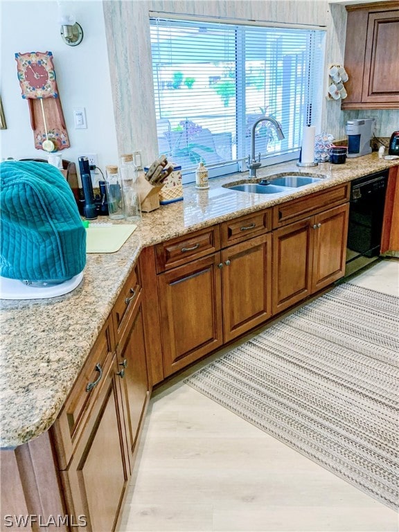 kitchen featuring light stone counters, black dishwasher, sink, and light hardwood / wood-style flooring