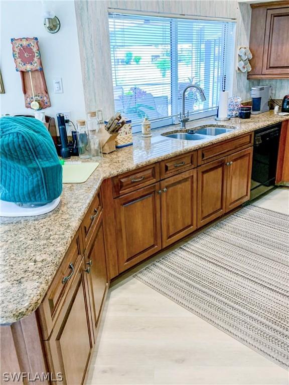 kitchen featuring dishwasher, light stone counters, brown cabinetry, and a sink