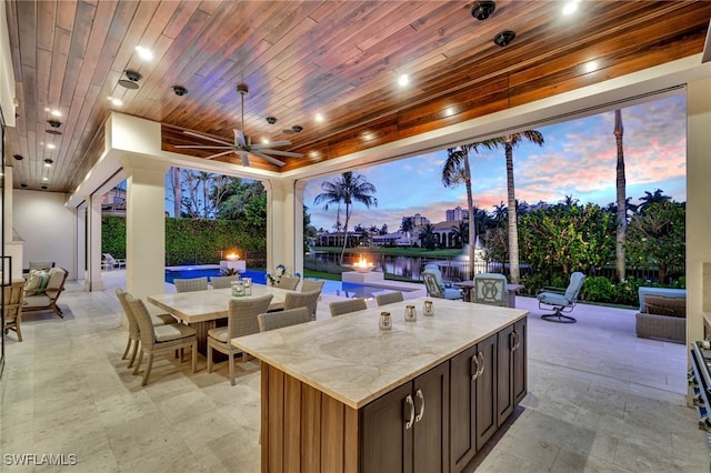 patio terrace at dusk featuring a water view and ceiling fan