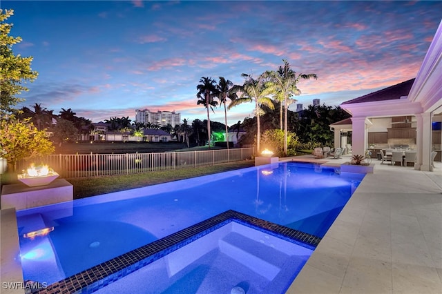 pool at dusk with a patio and an in ground hot tub