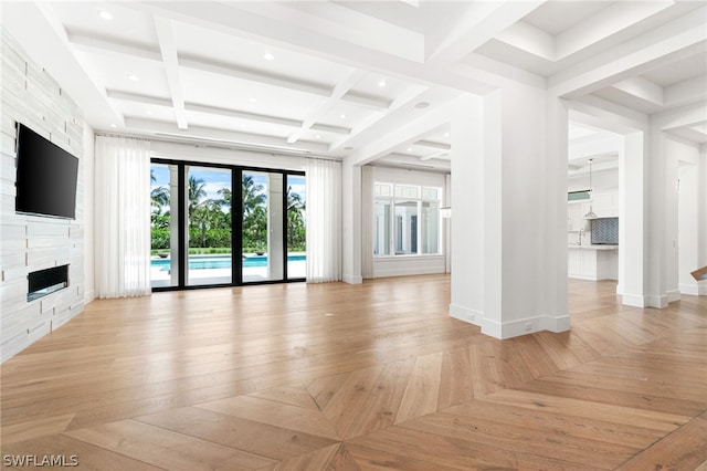 unfurnished living room with beam ceiling, light hardwood / wood-style flooring, a stone fireplace, and coffered ceiling