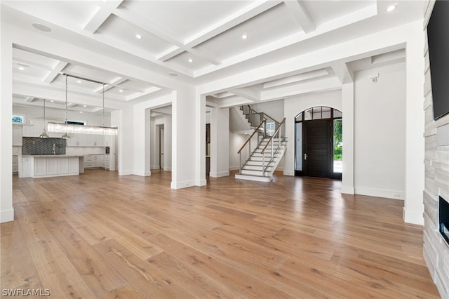 unfurnished living room featuring beam ceiling, light wood-type flooring, and coffered ceiling