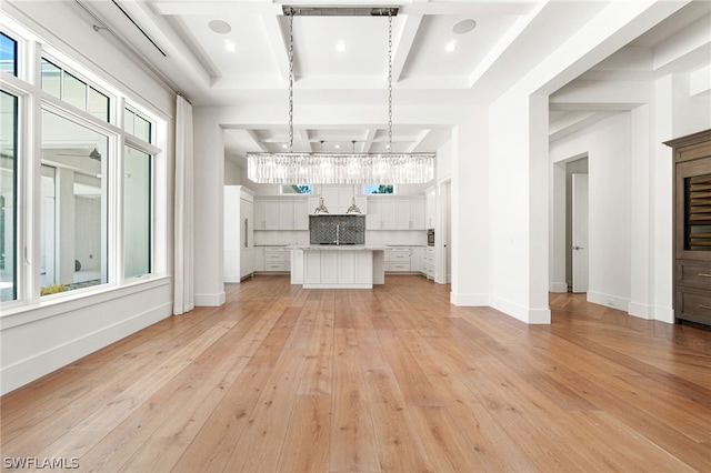 unfurnished living room with a chandelier, beamed ceiling, light hardwood / wood-style floors, and coffered ceiling