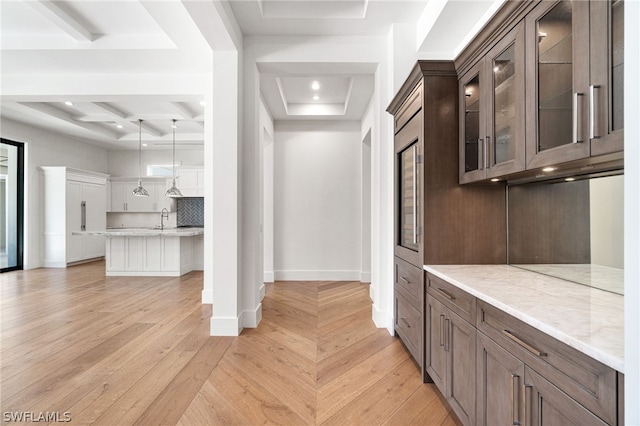 kitchen featuring dark brown cabinetry, a raised ceiling, light stone counters, light hardwood / wood-style flooring, and decorative backsplash