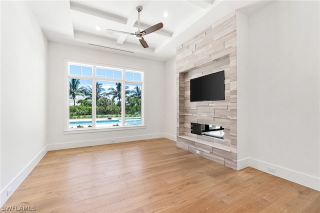 unfurnished living room featuring ceiling fan, coffered ceiling, a raised ceiling, a fireplace, and light wood-type flooring