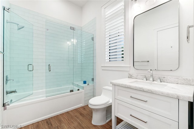 full bathroom featuring shower / bath combination with glass door, hardwood / wood-style floors, vanity, and toilet